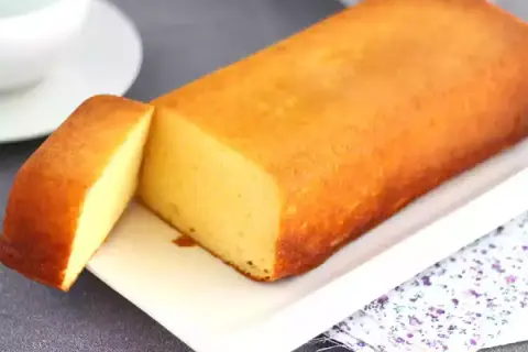 Un delicioso bizcocho de leche condensada, dorado y esponjoso, servido en una bandeja blanca con una porción cortada.