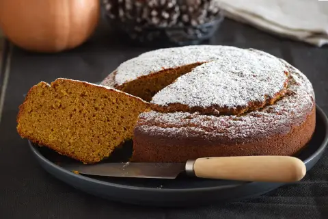 Dos rebanadas de bizcocho de calabaza apiladas, espolvoreadas con azúcar glas, con menta y tenedor.