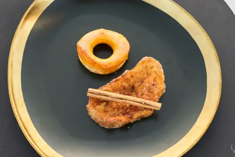 Rosquillas de Alcalá y torrija con canela, servidas en plato negro con borde dorado.