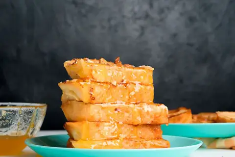 Torrijas de horchata doradas y jugosas, apiladas y bañadas en miel, con un cuenco de miel al lado.