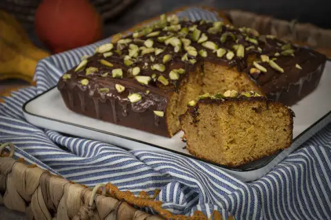 Bizcocho con harina de espelta, cubierto de chocolate y pistachos. Una rebanada muestra su interior esponjoso.