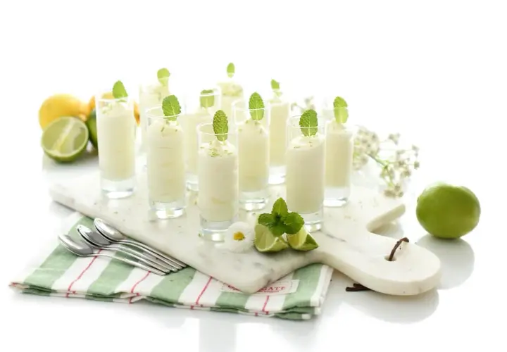Delicioso mousse de limón en vasitos, decorado con menta y ralladura de limón. Frescura y sabor en cada bocado.