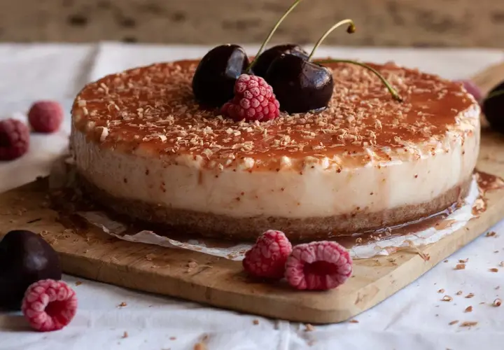 Tarta de queso con leche condensada, cubierta de mermelada y virutas de chocolate, decorada con cerezas y frambuesas.