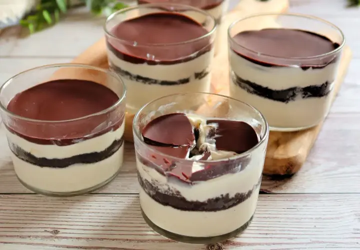 Cuatro vasitos de tiramisú de oreo, con capas de crema y galleta, cubiertos de chocolate.