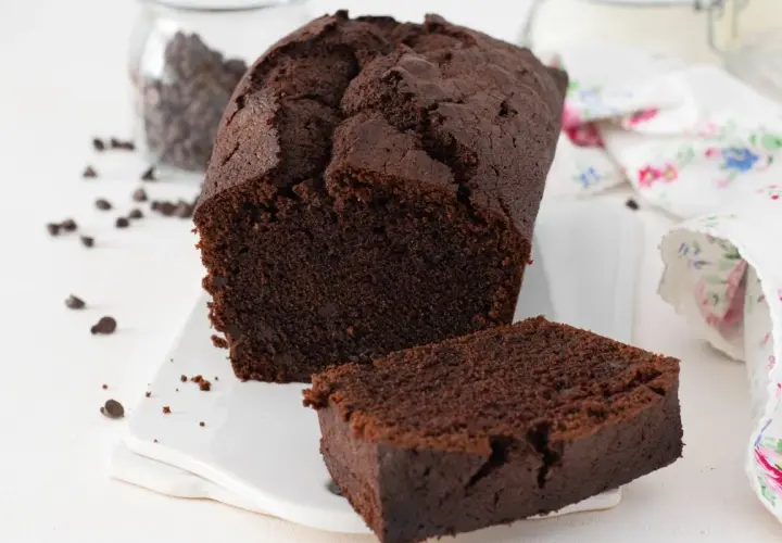 Un delicioso plum cake de chocolate, con una rebanada separada y chispas de chocolate esparcidas.