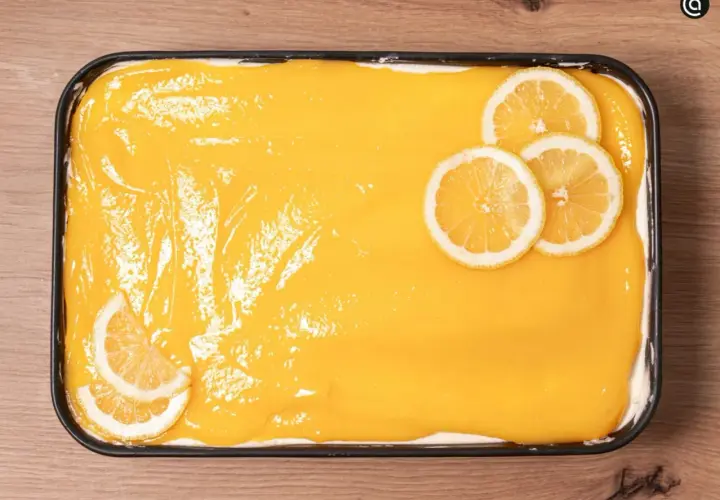 Un delicioso tiramisú de limón, cubierto con una crema amarilla brillante y decorado con rodajas de limón fresco.