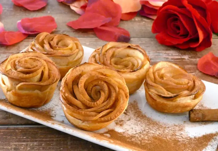 Deliciosas rosas de manzana horneadas, espolvoreadas con canela, junto a pétalos rojos y una rosa natural.