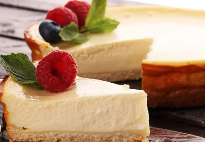 Una deliciosa tarta de queso, con una porción servida en un tenedor, decorada con frambuesas frescas y hojas de menta.