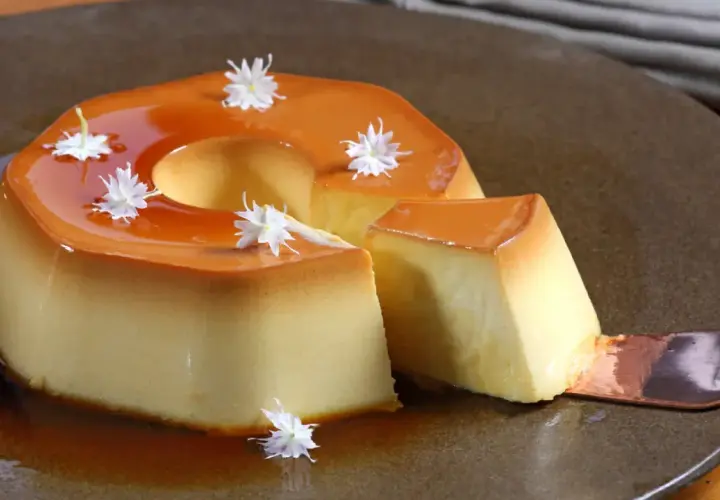 Delicioso flan de manzana con caramelo líquido y decorado con flores blancas. Una porción se sirve con una cuchara.