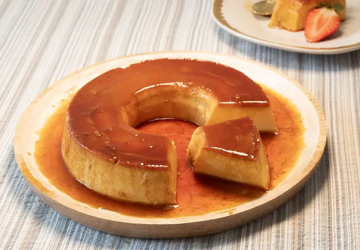 Un delicioso flan de leche condensada bañado en caramelo líquido, servido en un plato de madera.
