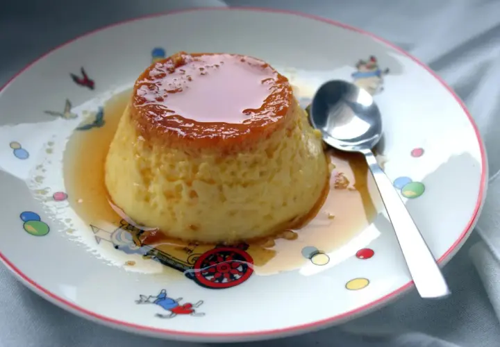 Delicioso flan de huevo casero con caramelo líquido, servido en un plato con dibujos infantiles.
