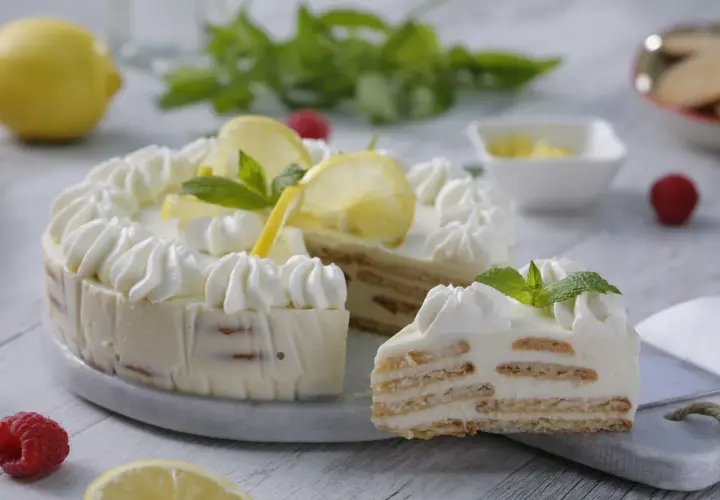 Deliciosa tarta de limón con leche condensada, decorada con crema batida, rodajas de limón y menta. Una rebanada muestra sus capas de galleta y crema.