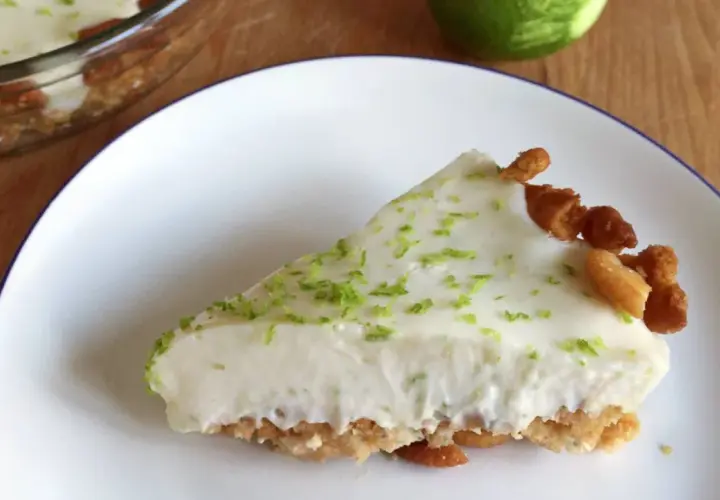 Rebanada cremosa de key lime pie, con ralladura de lima y trozos de galleta en el borde.