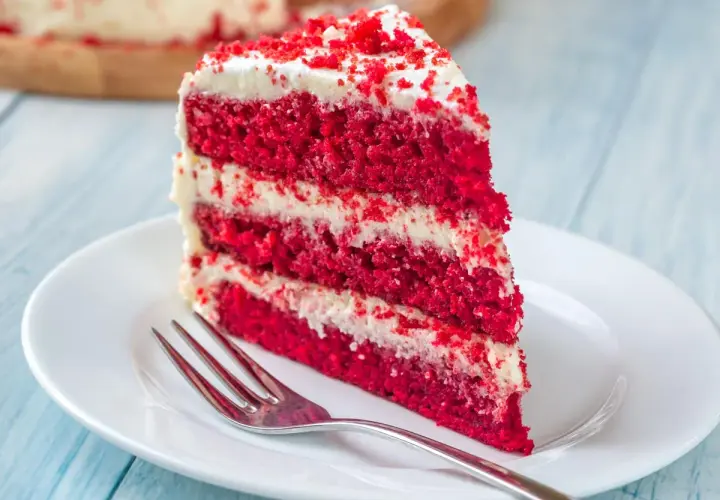 Rebanada de tarta red velvet con capas de bizcocho rojo y crema blanca, lista para disfrutar. Los ingredientes de esta tarta son un secreto delicioso.