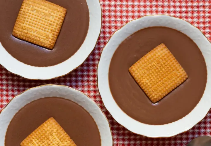 Tres cuencos de natillas de chocolate, cada uno con una galleta cuadrada encima, sobre un mantel de cuadros rojos y blancos.