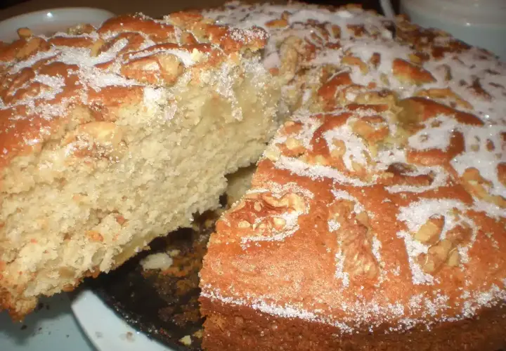 Un delicioso bizcocho de manzana y nueces, espolvoreado con azúcar, con una rebanada retirada.