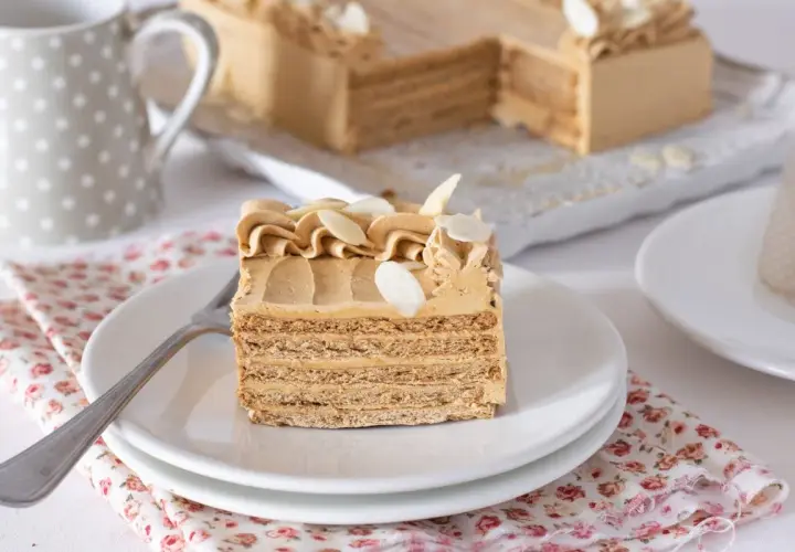 Deliciosa tarta de moka en capas, decorada con crema y almendras. Un trozo servido en plato blanco, listo para disfrutar.