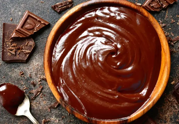 Un cuenco de madera lleno de cremoso de chocolate, con trozos de chocolate y virutas esparcidos alrededor.
