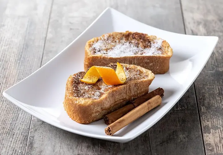 Dos deliciosas torrijas, con azúcar y canela, decoradas con piel de naranja y varas de canela. El mejor pan para torrijas, esponjoso y dorado.