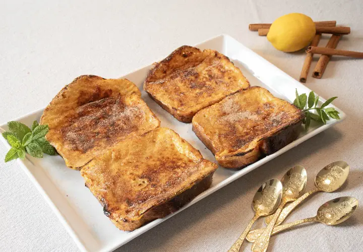 Cuatro deliciosas torrijas al horno, espolvoreadas con azúcar y canela, listas para disfrutar.