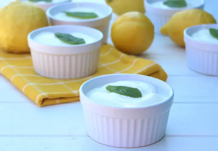 Delicioso mousse de limón mambo en ramequines blancos, adornado con hojas de menta. Limones frescos y una servilleta amarilla completan la escena.