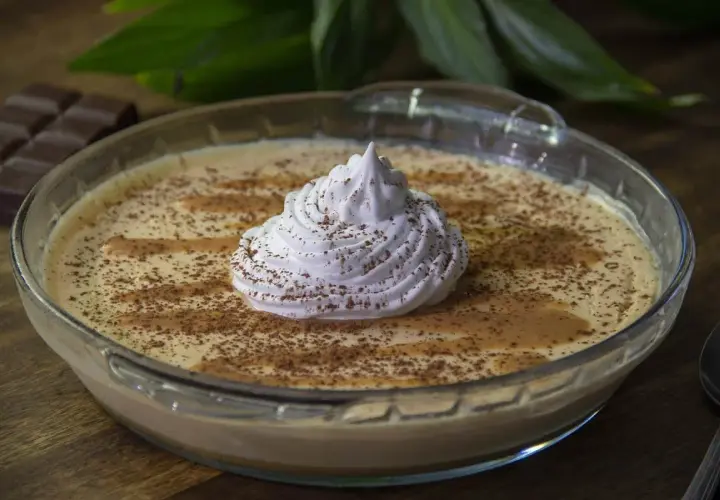 Delicioso mousse de dulce de leche en un bol de vidrio, coronado con crema batida y espolvoreado con cacao.