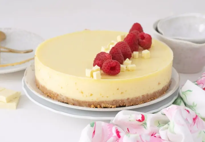 Deliciosa tarta de chocolate blanco adornada con frambuesas frescas y trocitos de chocolate.