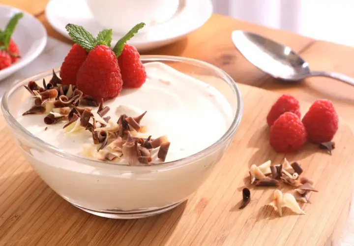 Delicioso mousse de chocolate blanco adornado con frambuesas frescas y virutas de chocolate.