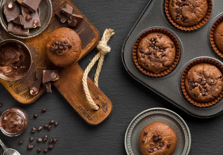 Deliciosos muffins de chocolate recién horneados, algunos en molde y otros listos para disfrutar, acompañados de trozos de chocolate y crema.