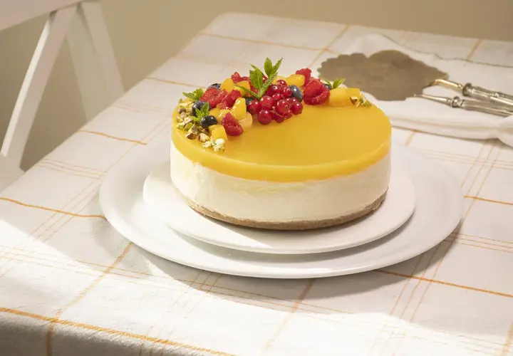 Deliciosa tarta de mango y queso, cubierta con gelatina amarilla y decorada con frutos rojos y pistachos.