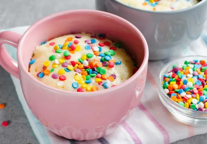 Un delicioso bizcocho al microondas en una taza rosa, cubierto de coloridas chispas. ¡Listo para disfrutar en minutos!