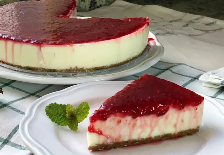 Deliciosa tarta de yogur sin horno cubierta con mermelada de frutos rojos. Un trozo servido con menta fresca.