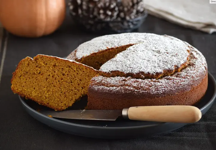 Dos rebanadas de bizcocho de calabaza apiladas, espolvoreadas con azúcar glas, con menta y tenedor.