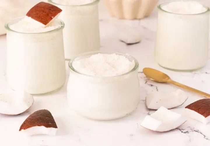 Delicioso mousse de coco en vasitos de cristal, decorado con coco rallado y trozos de coco fresco.