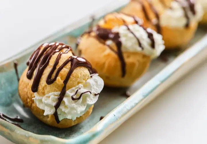 Profiteroles rellenos de crema y bañados en chocolate, perfectos para tu próxima receta.