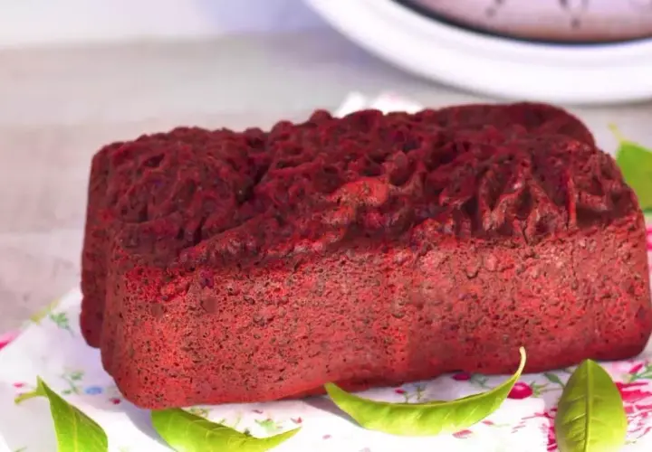 Un delicioso pan de red velvet, con una textura esponjosa y un color vibrante, decorado con hojas verdes sobre un mantel floral.