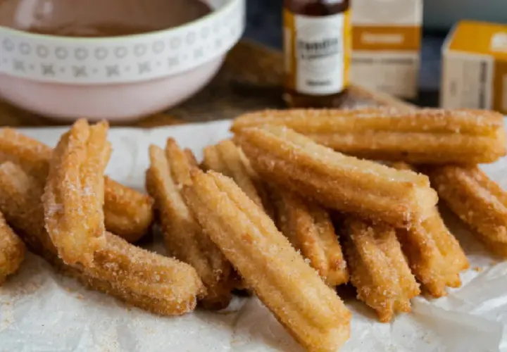 Montón de churros caseros recién hechos, espolvoreados con azúcar y canela, listos para mojar en chocolate caliente.