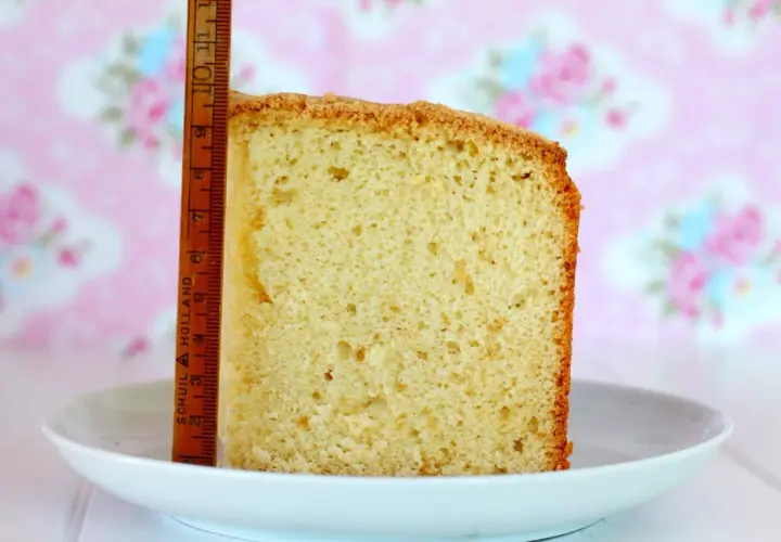 Rebanada de bizcocho de vainilla esponjoso, medido con una regla de madera. Fondo rosa con flores.