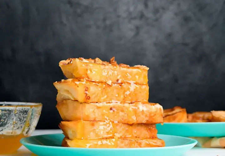 Torrijas de horchata doradas y jugosas, apiladas y bañadas en miel, con un cuenco de miel al lado.