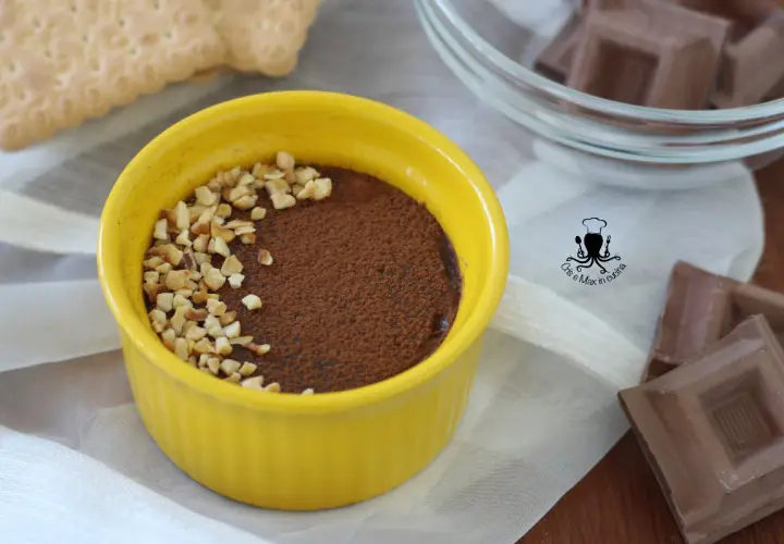 Pudín de chocolate cremoso en un cuenco amarillo, espolvoreado con cacao y nueces picadas.