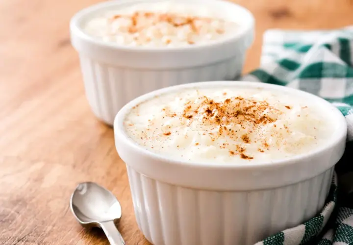 Dos ramequines de arroz con leche en microondas, espolvoreados con canela, sobre una mesa de madera.