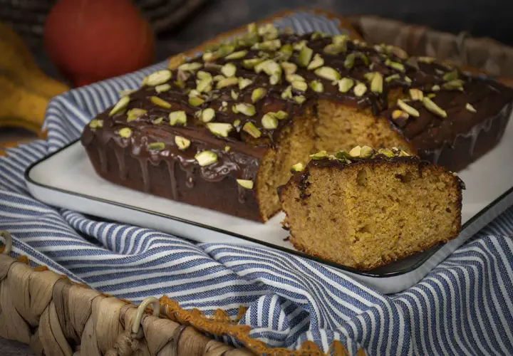 Bizcocho con harina de espelta, cubierto de chocolate y pistachos. Una rebanada muestra su interior esponjoso.