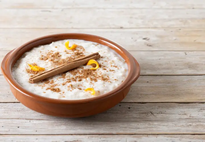 Un tazón de arroz con leche cremoso, espolvoreado con canela y adornado con cáscara de naranja y una rama de canela. ¡Perfecto para tu receta de arroz con leche cremoso!