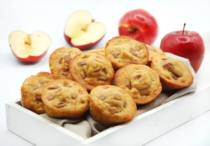 Deliciosas magdalenas de manzana, recién horneadas y listas para disfrutar. Dos manzanas rojas enteras y dos cortadas a la mitad acompañan esta tentación.