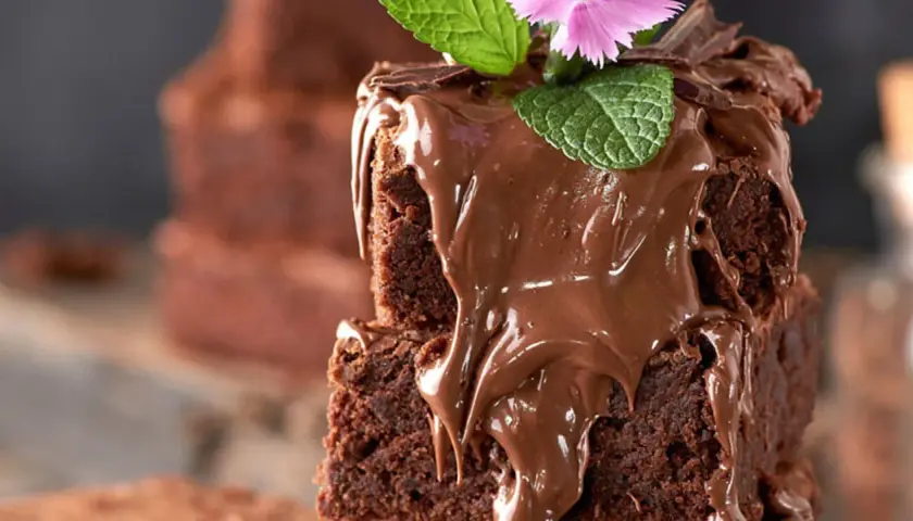 Delicioso brownie esponjoso cubierto de chocolate derretido, menta y una flor rosa. ¡Perfecto para tu próxima receta de brownie esponjoso!