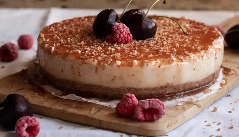 Tarta de queso con leche condensada, cubierta de mermelada y virutas de chocolate, decorada con cerezas y frambuesas.