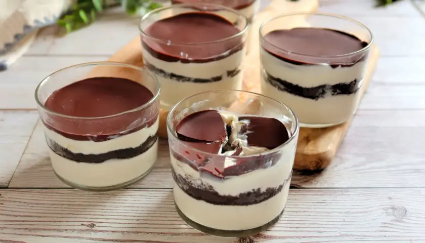 Cuatro vasitos de tiramisú de oreo, con capas de crema y galleta, cubiertos de chocolate.