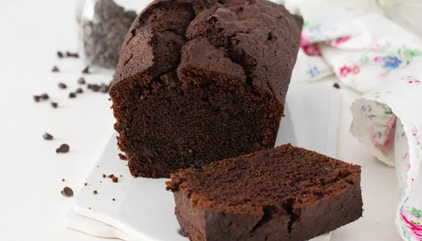 Un delicioso plum cake de chocolate, con una rebanada separada y chispas de chocolate esparcidas.
