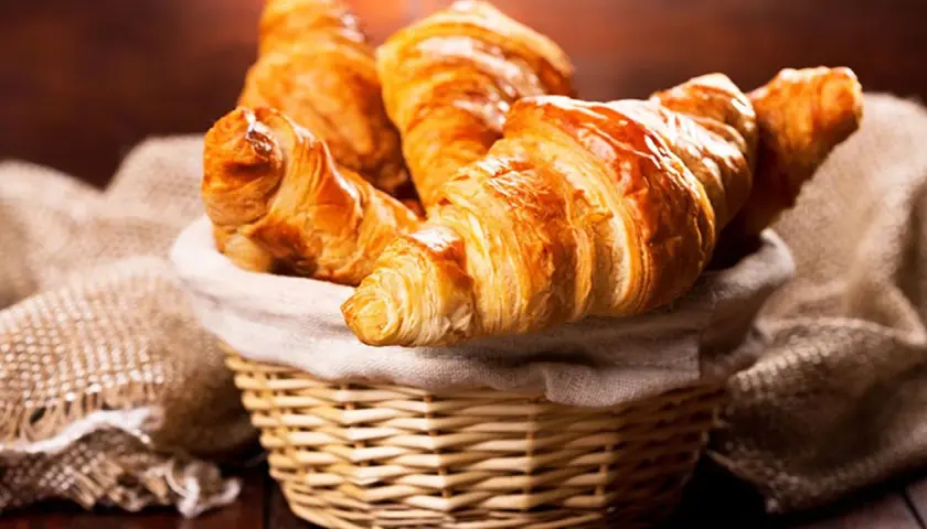 Cesta de mimbre llena de deliciosos croissants caseros, dorados y crujientes, listos para disfrutar.