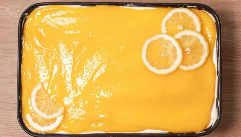 Un delicioso tiramisú de limón, cubierto con una crema amarilla brillante y decorado con rodajas de limón fresco.